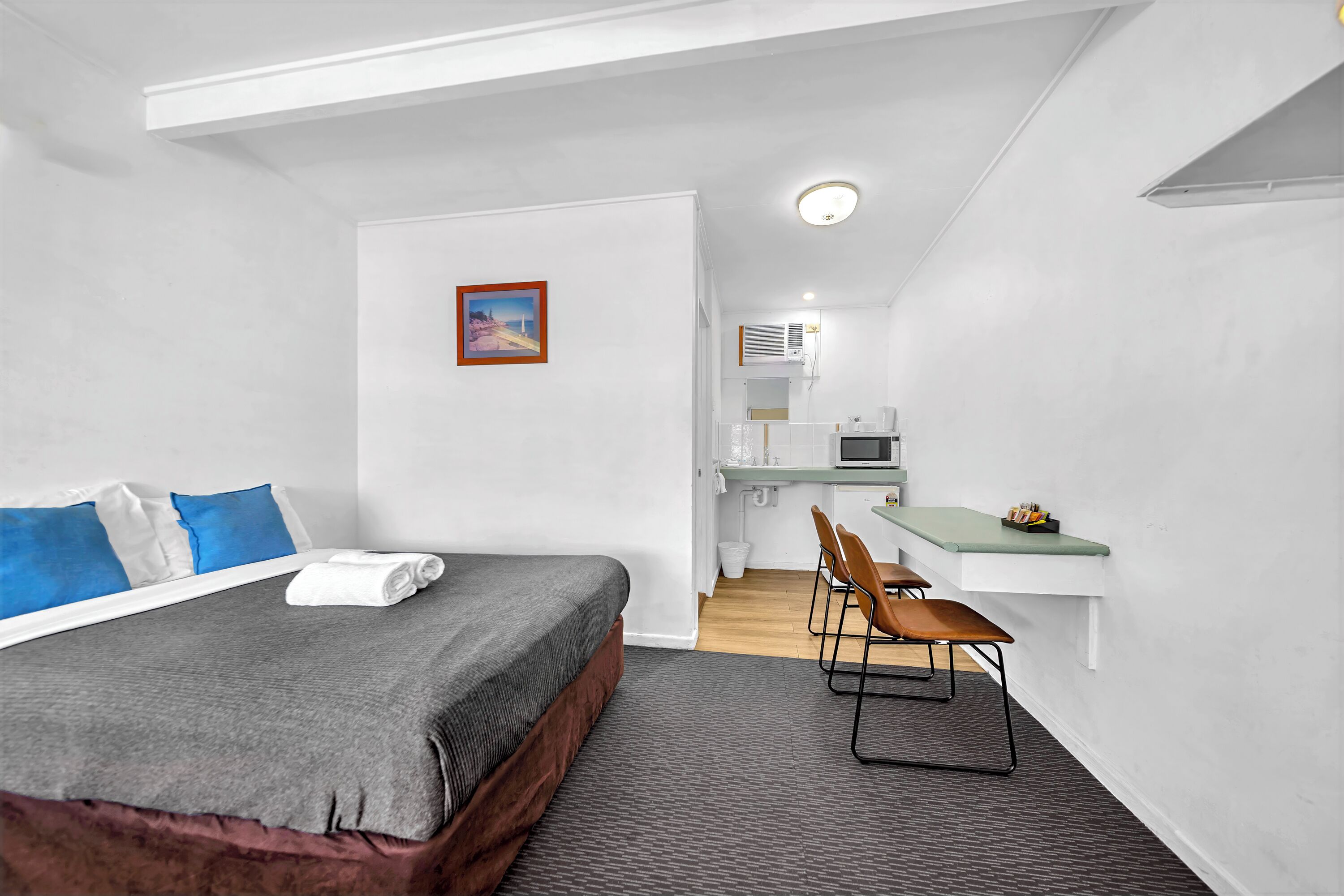 Una habitación de hotel compacta con cama, escritorio y kitchenette.