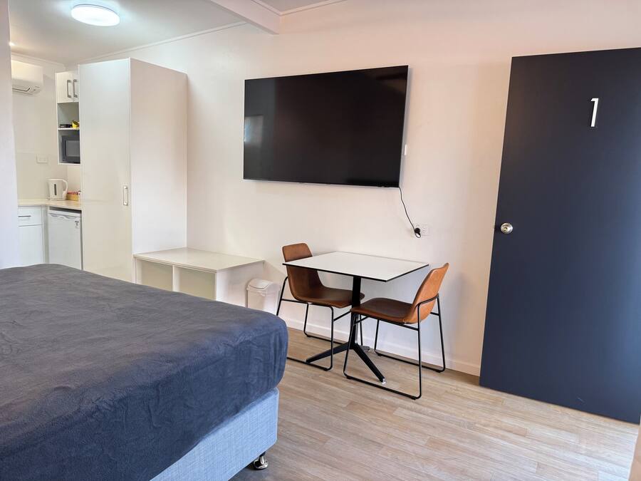 Ein modernes Zimmer mit einem Bett, einem Schreibtisch mit zwei Stühlen, einem Flachbildfernseher, einem Kleiderschrank und einer Tür mit der Nummer 1.