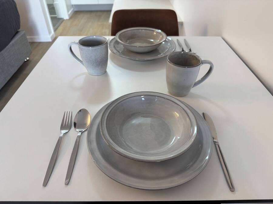 Taula de dinar arrodonida amb plats, cuinells, una tassa i coberts.