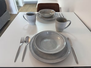 Ein Esstisch ist mit Tellern, Schüsseln, einer Tasse und Besteck gedeckt.
