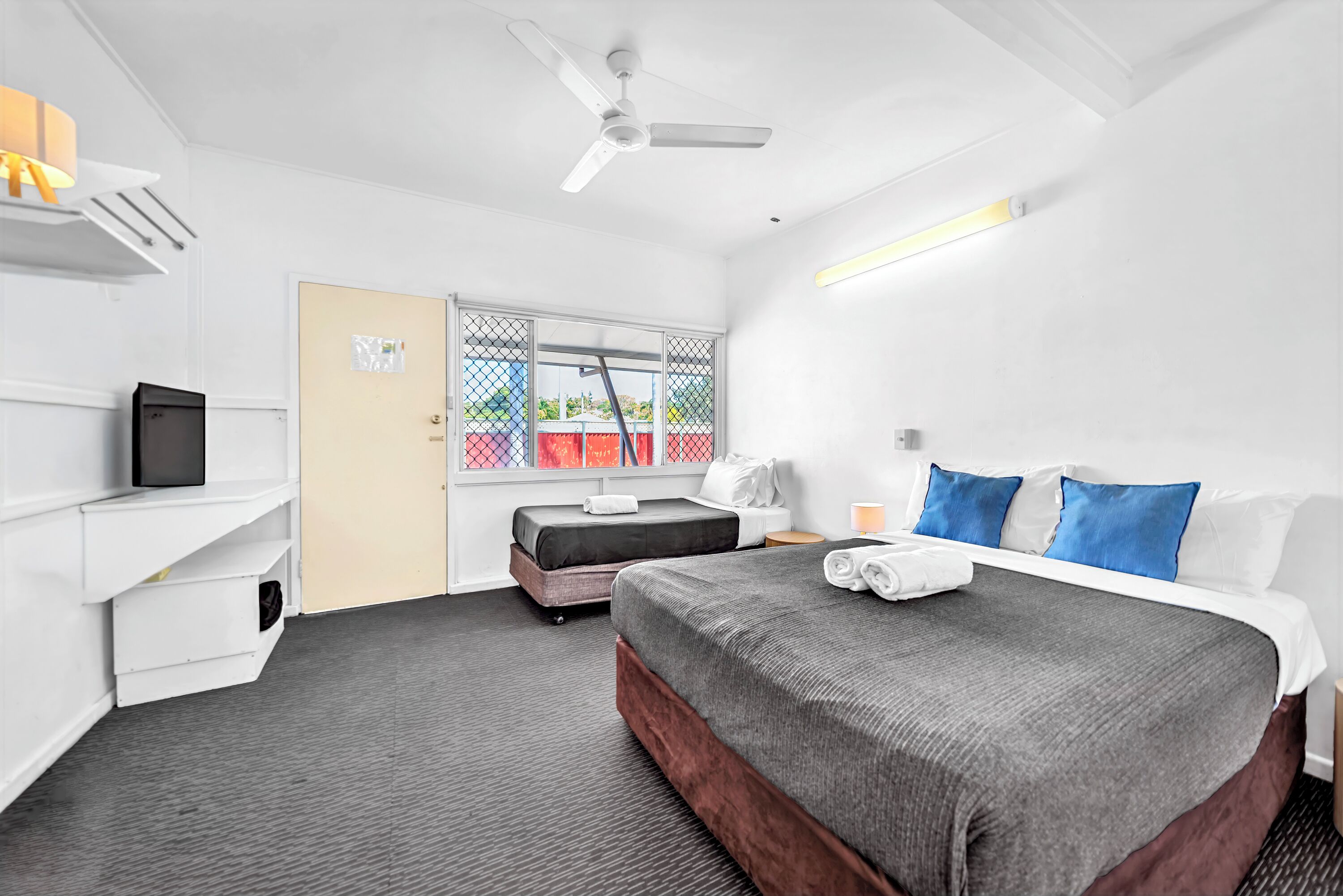 A hotel room with a bed, bedside table, and a desk with a computer.