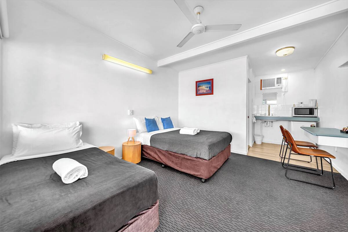 A hotel room with two beds, a desk, a chair, a microwave, and a ceiling fan.
