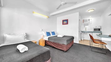 A hotel room with two beds, a desk, a chair, a microwave, and a ceiling fan.