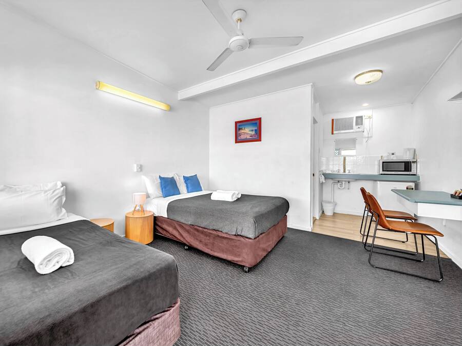 A hotel room with two beds, a desk, a chair, a microwave, and a ceiling fan.