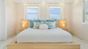 A bedroom with a large bed, two bedside lamps, and a view of the city through two windows. - Ponton 34-g (Oranjestad)