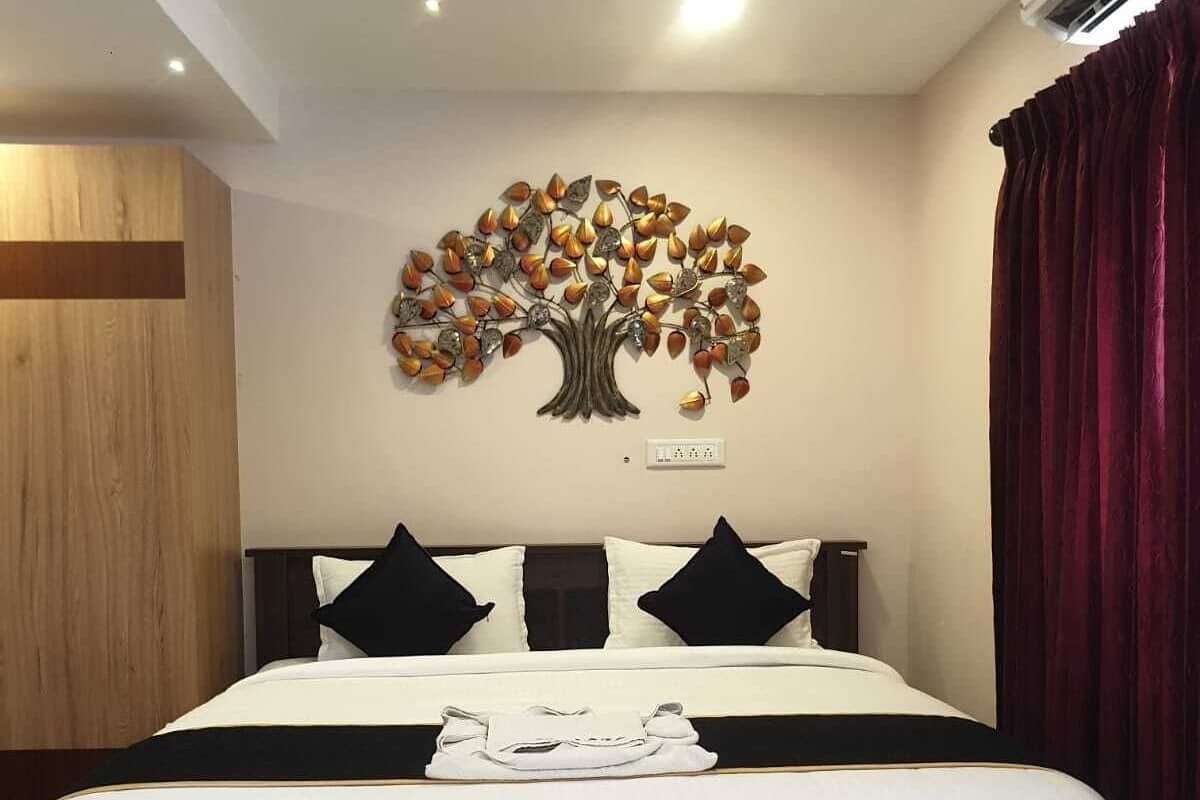 Una cama bien tendida con sábanas blancas y almohadas negras, un adorno de árbol en la pared y una cortina roja.