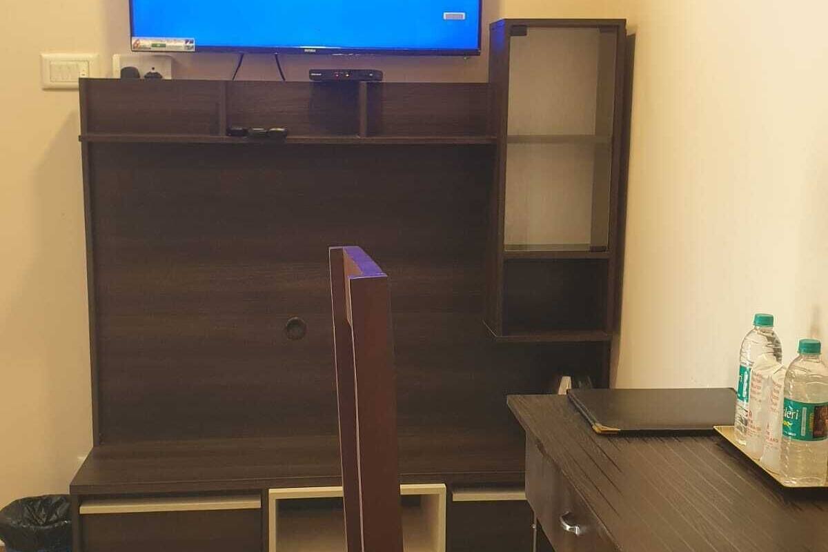 Una habitación con un mueble de entretenimiento de madera oscura, un televisor encima, un escritorio con una silla y dos botellas de agua sobre el escritorio.