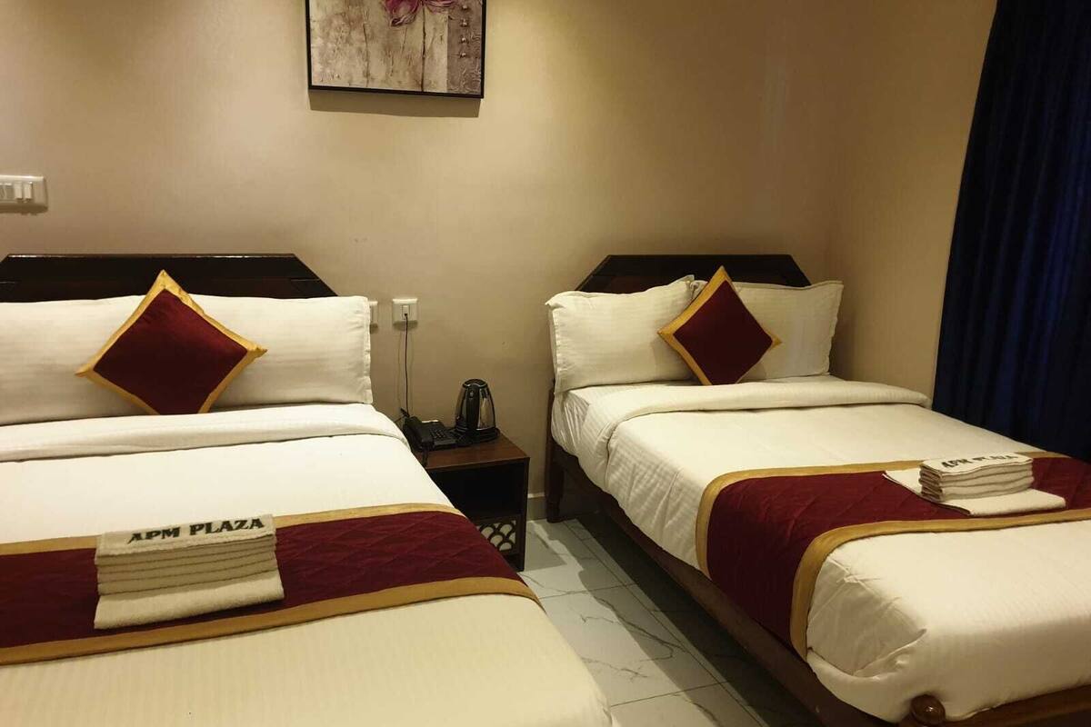Habitación de hotel con dos camas, cada una con ropa blanca y detalles burdeos, una mesita de noche con teléfono y lámpara, y un cuadro colgado en la pared.