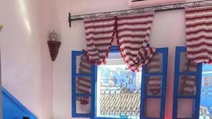 Une chambre avec une couvre-lit rouge, une serviette en forme de cygne et des rideaux à rayures.