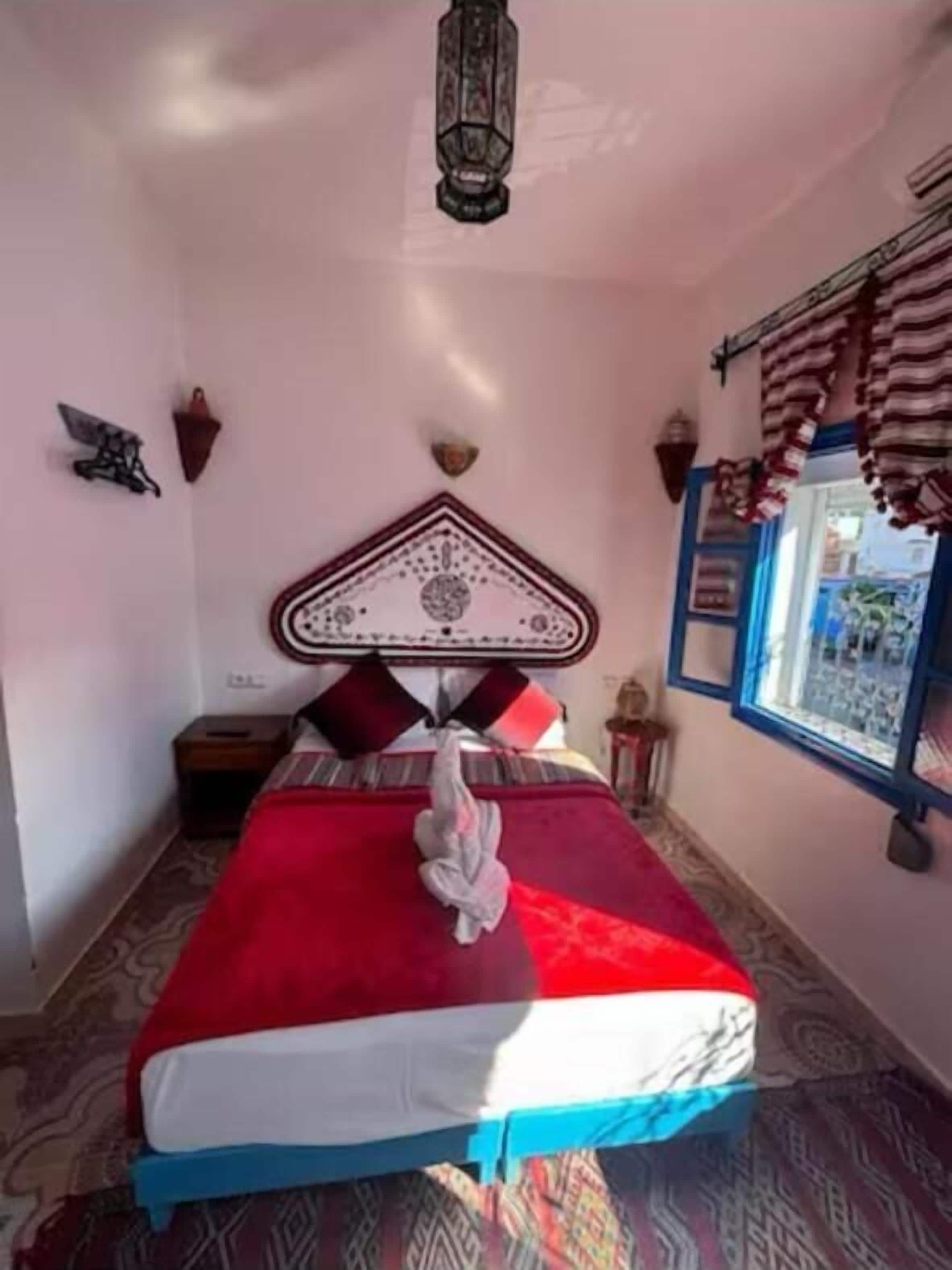 Ein Schlafzimmer mit einem Bett, einem Nachttisch, einer Wandleuchte und einem Fenster mit Vorhängen.
