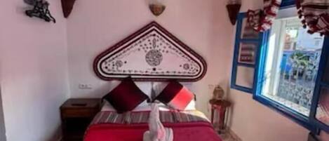 A bedroom with a bed, a nightstand, a wall-mounted lamp, and a window with curtains.