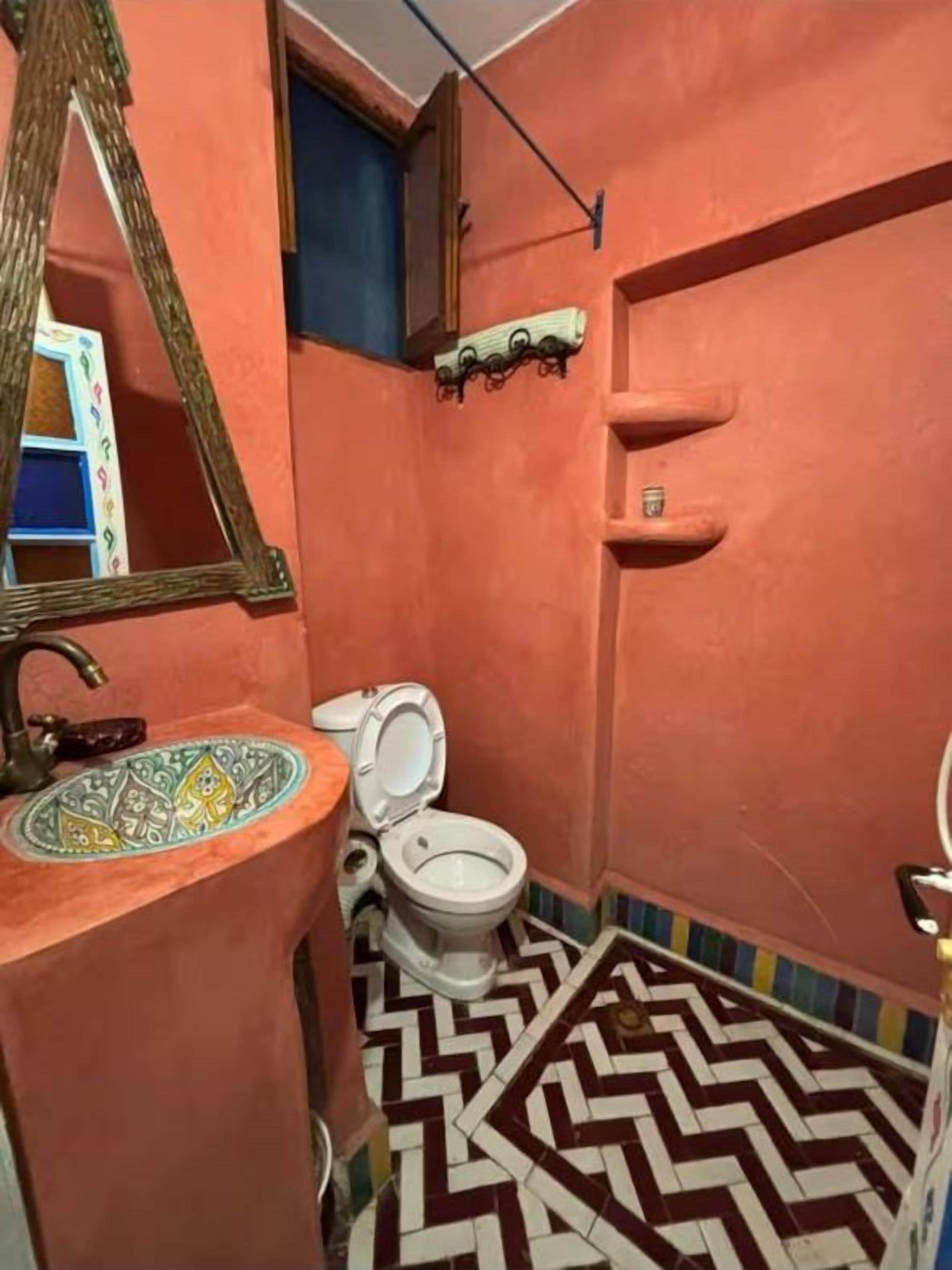 Un baño con pared rosa, inodoro blanco, lavamanos con azulejos decorativos y un espejo.