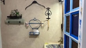 Une petite salle de bain comprenant des toilettes, un lavabo et une douche. On y trouve des étagères avec des articles de toilette et un porte-serviettes.