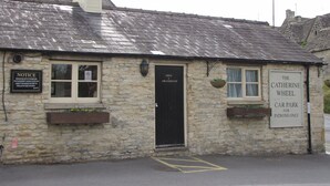 Un bâtiment en pierre avec une porte noire, un panneau d’information et un panneau indiquant : « Parking de The Catherine Wheel, réservé aux clients ».
