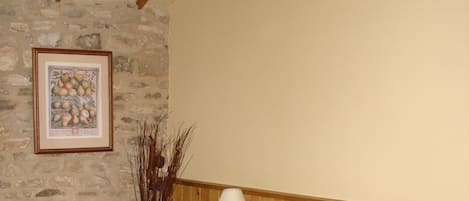 A bedroom with a stone wall, a wooden headboard, a bedside table with a lamp, a telephone, and a floral pillow.