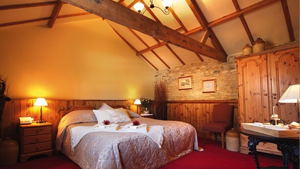 Une chambre confortable avec un grand lit, des poutres en bois, un mur en pierre et une moquette rouge.