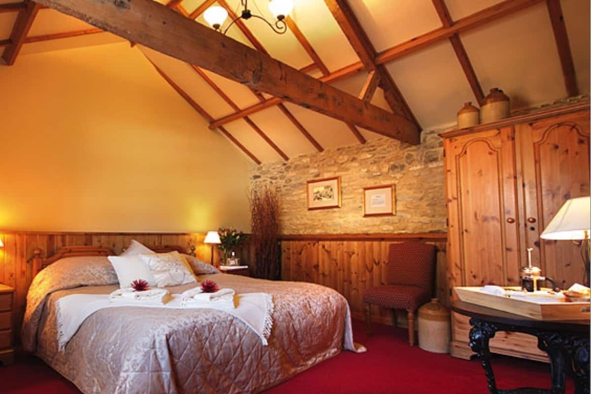 A cozy bedroom with a large bed, wooden beams, stone wall, and a red carpet.