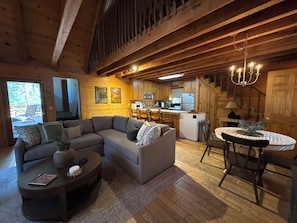 A cozy cabin interior with a sectional sofa, a dining table, and a kitchen area.