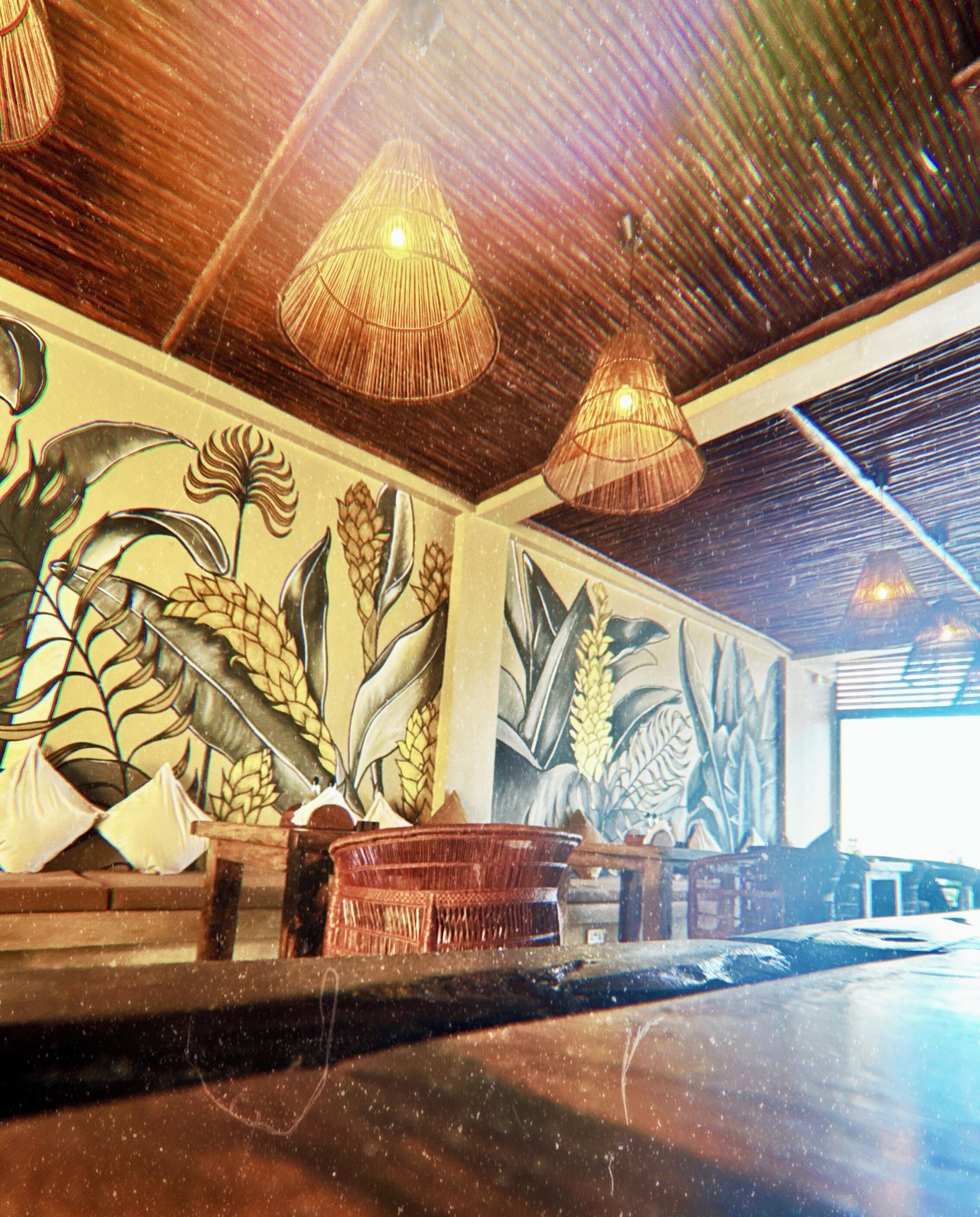 A room with a large mural of tropical plants, wooden ceiling beams, and hanging wicker lamps.