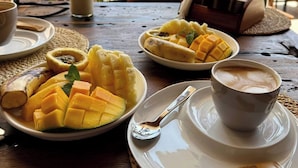 Una mesa con un plato de mango en rodajas, una taza de café y un vaso de leche.