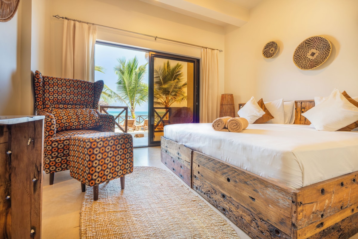 Un dormitorio con cama, una silla, un cofre de madera y vistas a la playa.
