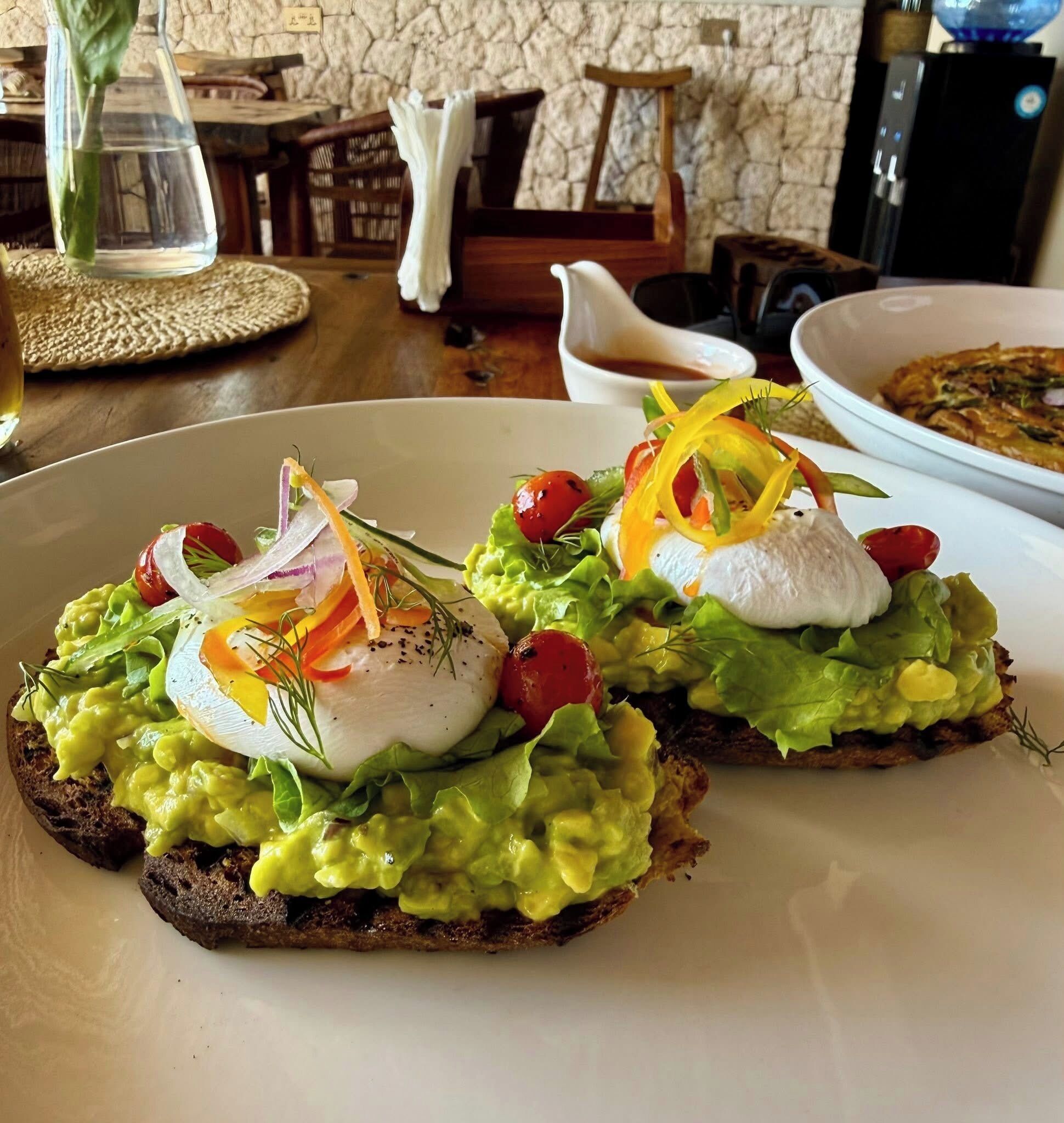 Un tavolo da pranzo con una fetta di pane tostato all'avocado, guarnita con uova in camicia e verdure.