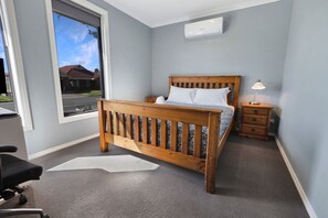 Une chambre à coucher avec un lit en bois, une table de chevet, une lampe et une fenêtre donnant sur une maison.