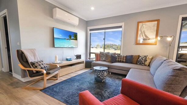 Un moderno salón con un sofá, un sillón rojo y un televisor que muestra una escena de playa.