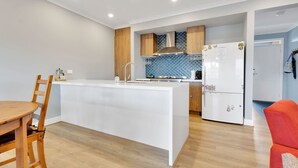 Una cocina moderna con una isla central, armarios de madera, un protector contra salpicaduras azul y un refrigerador blanco.