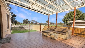 Un patio techado al aire libre con piso de madera, un sofá de mimbre y una estructura de techo de vidrio.