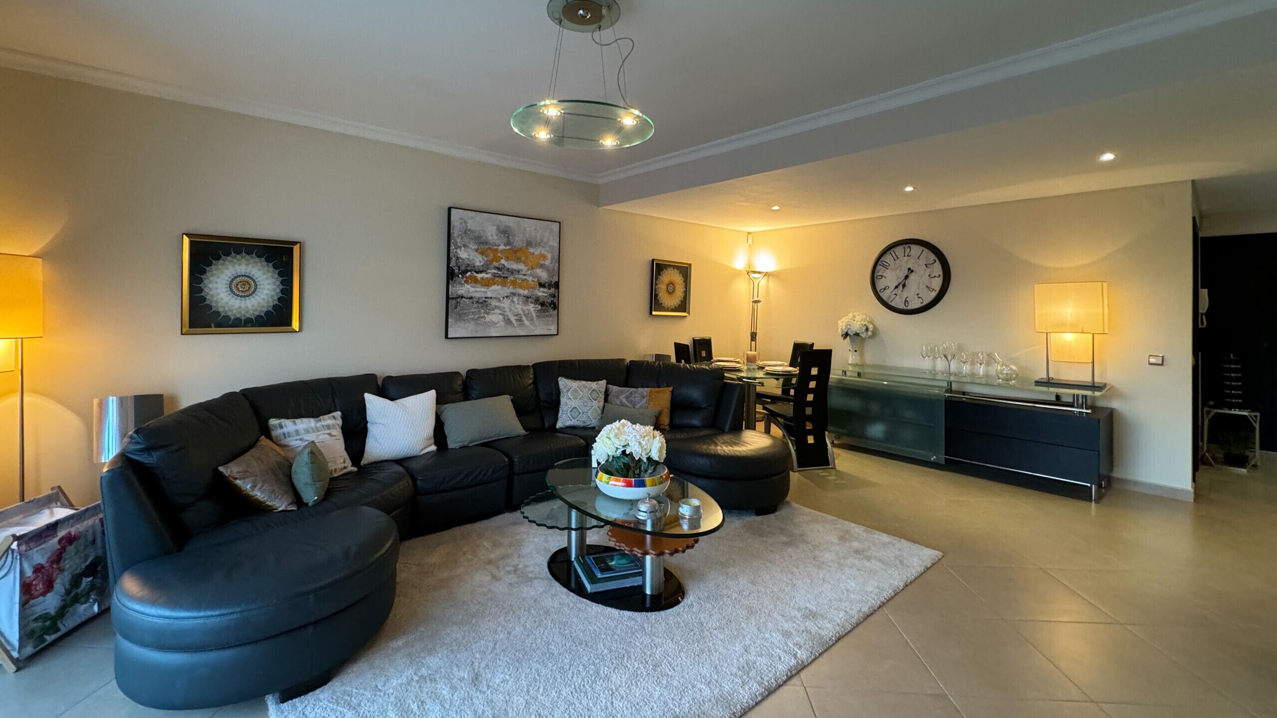Ein modernes Wohnzimmer mit einer schwarzen Ledersofa, einem Glastisch und einem Essbereich mit Tisch und Stühlen mit Glastisch.