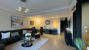 Una sala de estar moderna con un sofá negro, una mesa de centro de vidrio y un comedor con una mesa y sillas de vidrio.