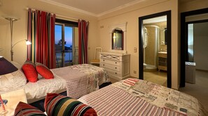 Habitación de hotel con dos camas, un tocador, un espejo y un baño visible a través de una puerta abierta.