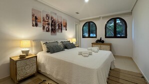 Un dormitorio con una cama grande, dos mesitas de noche y un ventanal con vistas a árboles.