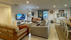 Una sala de estar moderna con un sofá, un banco de madera, un televisor y un comedor con sillas y una mesa.
