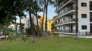 Un edificio de varios pisos con balcones, rodeado de árboles y un espacio con césped.