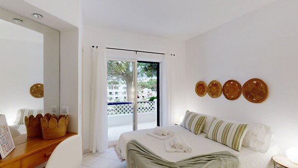 Une chambre à coucher avec un lit, une table de chevet en bois, un miroir et une vue sur le balcon extérieur.