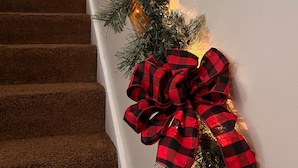 A staircase with a garland and a large red and black checkered bow.