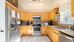 A kitchen with wooden cabinets, stainless steel appliances, a tiled backsplash, and a window with a view.
