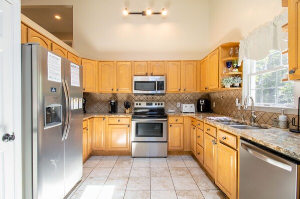 A kitchen with wooden cabinets, stainless steel appliances, a tiled backsplash, and a window with a view.