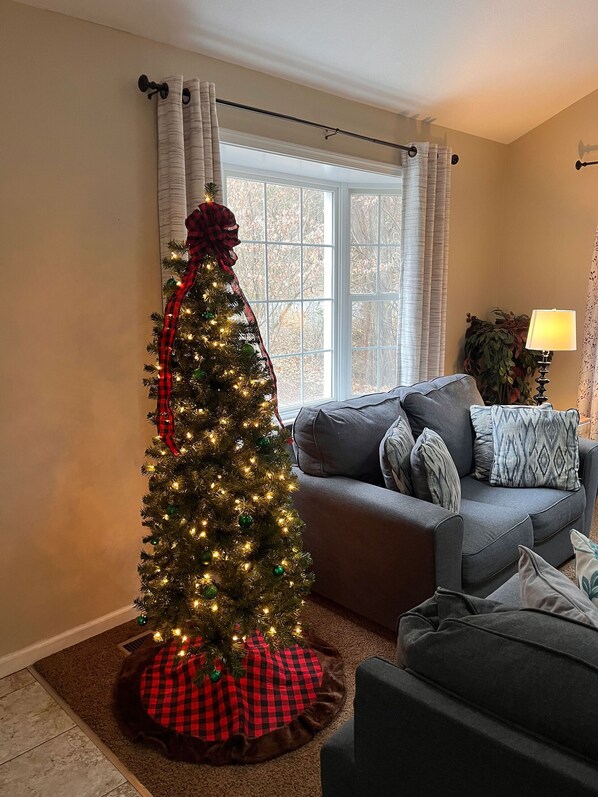 Un salon avec un sapin de Noël, un canapé gris et une lampe.