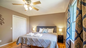 A bedroom with a bed, a ceiling fan, a nightstand, and a window with curtains.