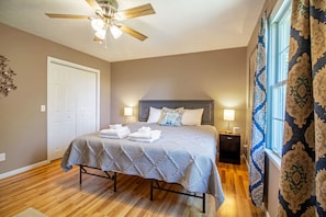 Une chambre à coucher avec un lit, un ventilateur de plafond, une table de chevet et une fenêtre avec des rideaux.