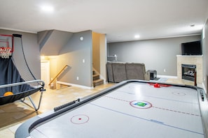 Una habitación con mesa de juego de bolos, aro de baloncesto y chimenea.