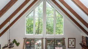 A room with a sloped ceiling, large windows, and a view of trees. - Ski Slope Views, Fireplace, Game Room & Loft Retreat (Mc Gaheysville)