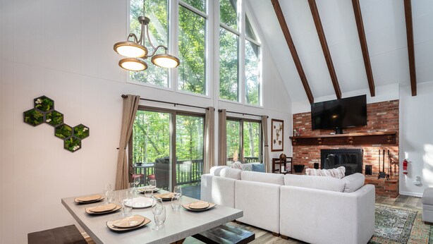A modern living room with a white sofa, dining table set for four, and a fireplace. - Ski Slope Views, Fireplace, Game Room & Loft Retreat (Mc Gaheysville)