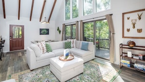 A spacious living room with a large sectional sofa, a coffee table, and a bookshelf. There is a large window providing a view of the outdoors. - Ski Slope Views, Fireplace, Game Room & Loft Retreat (Mc Gaheysville)