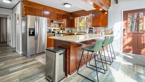 A modern kitchen with wooden cabinets, stainless steel appliances, and a bar area with stools. - Ski Slope Views, Fireplace, Game Room & Loft Retreat (Mc Gaheysville)