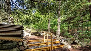 A wooden staircase leading up to a cabin in a forested area with a stone wall and wooden planks on the sides. - Modern-Lux Ski Retreat-Fireplace-Hot Tub-Space! (Mc Gaheysville)