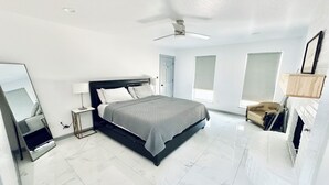 A modern bedroom with a large bed, a ceiling fan, a fireplace, and a mirror.